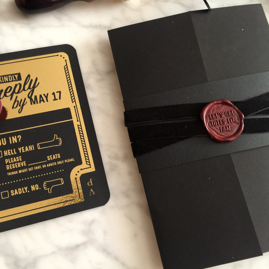 Overhead closeup of wedding invitations gold foil on black with velvet ribbon wrap